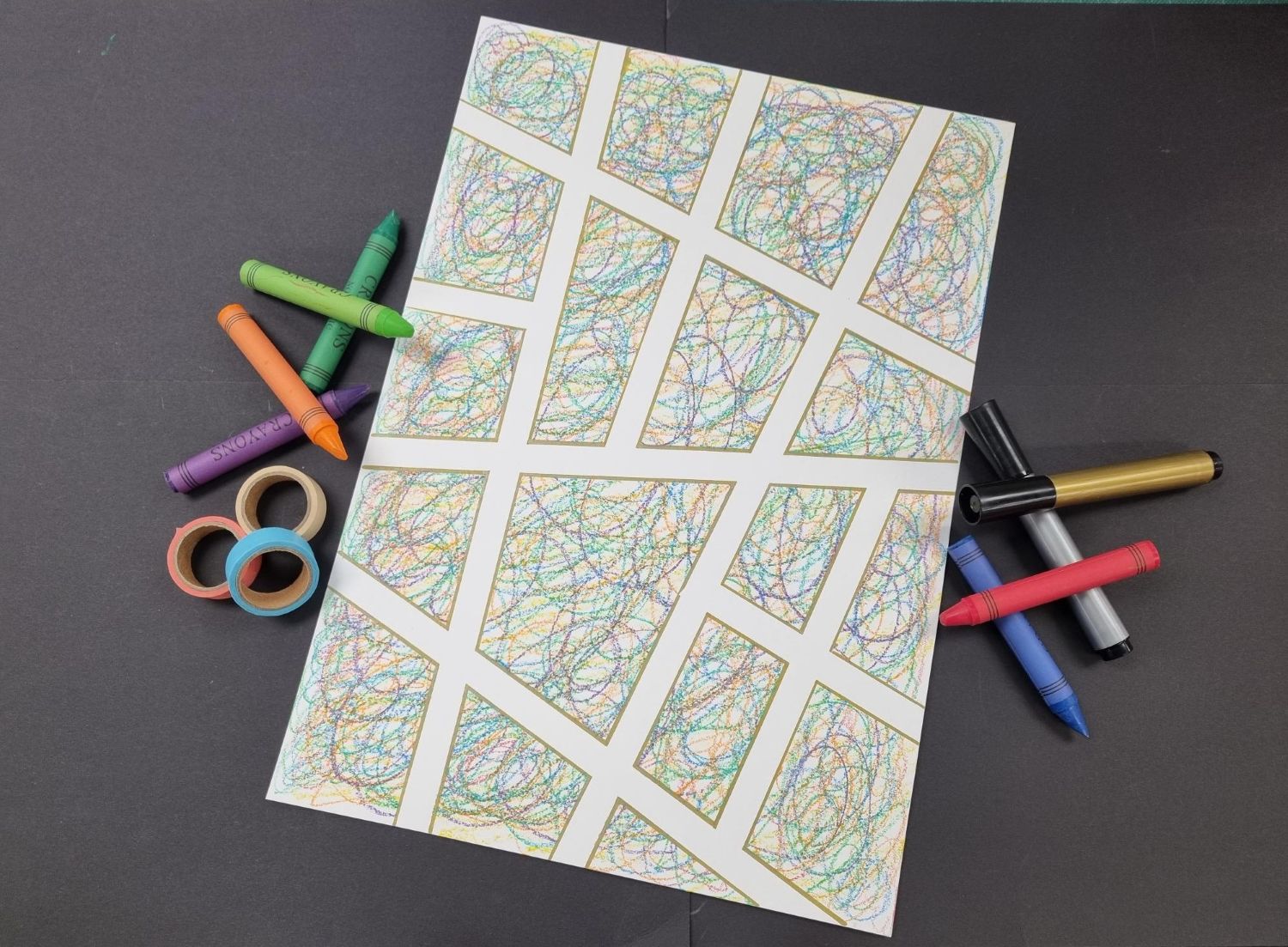 A creative art project laid out on a black background. At the center is a sheet of white paper featuring a finished tape-resist artwork displayed next to scattered crayons, markers, and rolls of tape.